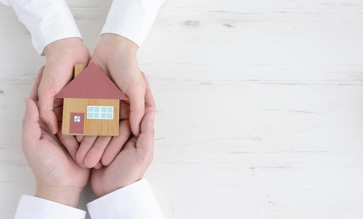 Quatre mains tenant une petite maquette d'une maison.