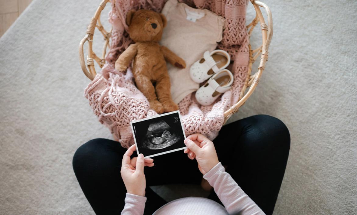 Femme enceinte regardant son échographie avec des affaires de nouveaux né