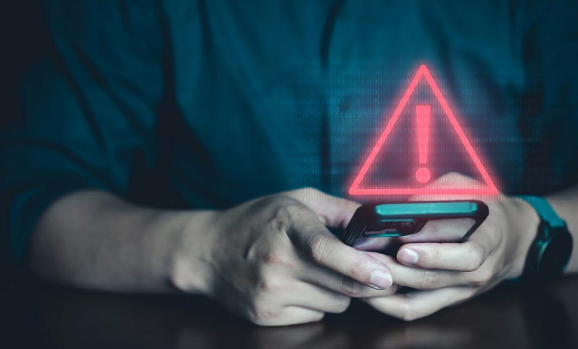 Un homme tenant son téléphone avec un symbole "attention" rouge.