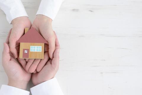 Quatre mains tenant une petite maquette d'une maison.