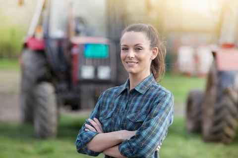 Jeune femme agricultrice avec des tracteurs en arrière plan.