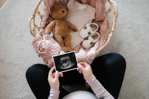 Femme enceinte regardant son échographie avec des affaires de nouveaux né