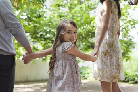 Deux adultes tenant la main d'une petite fille.